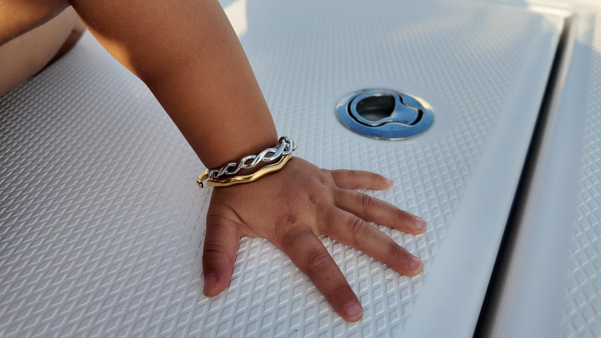 Slim gold Penny Faye bangle on a hand resting on a boat deck